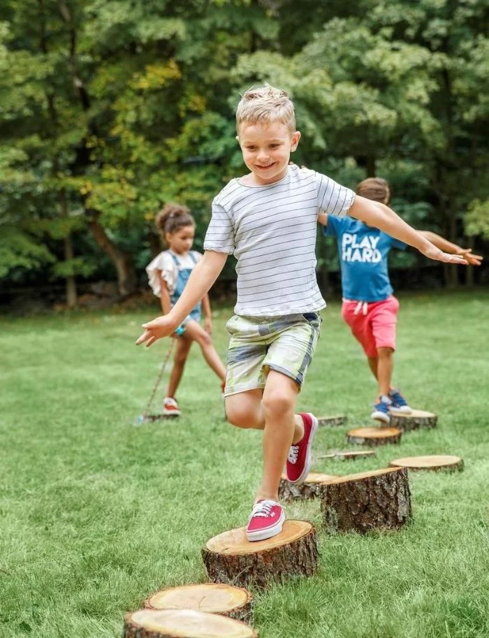 two boys and girl running on wooden logs outdoor activities for kids spread across field covered with grass