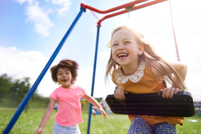 two girls playing on a swing set things to do outside one of them on the swing smiling