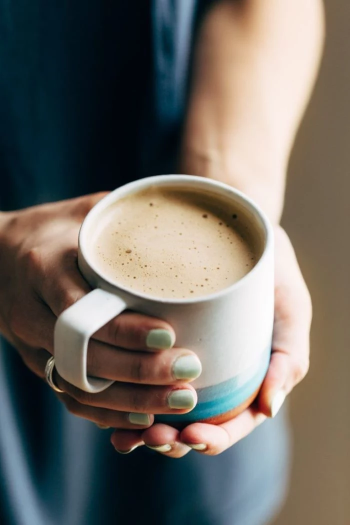 woman holding ceramic mug with turquoise nail polish coffee to water ratio cashew latte with milk foam