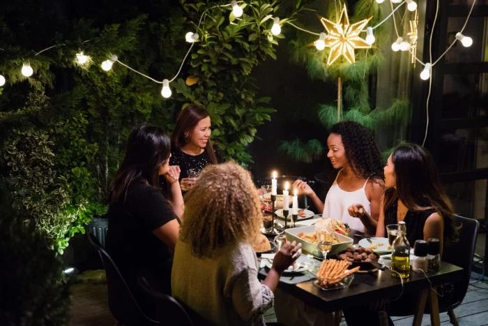 women sitting around table dining how to hang outdoor string lights strings of lights hanging from bushes around them