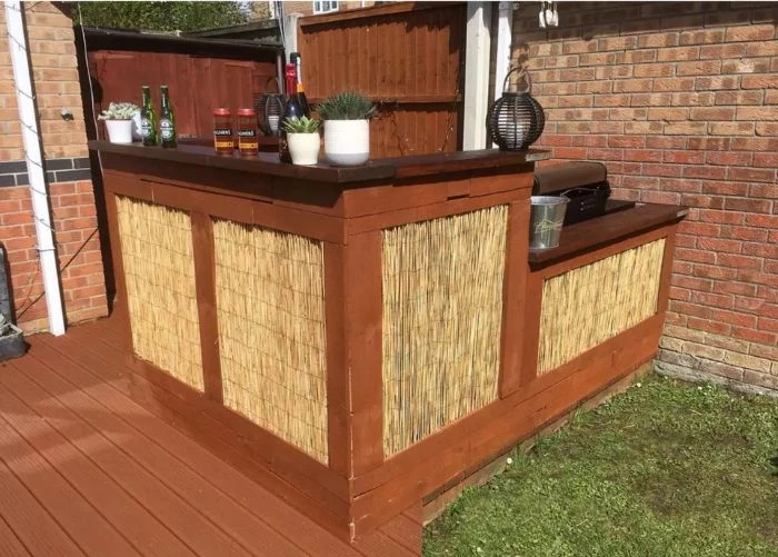 wooden bar with hay decorations on two levels different bottles plants on it outdoor wooden bar