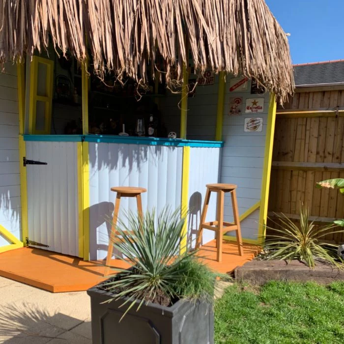 yellow and blue enclosure with dried palm leaves on the roof backyard tiki bar two wooden bar stools