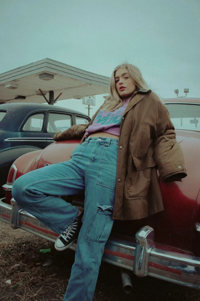 blonde girl leaning on car women fashion for summer 2021 wearing oversized jacket jeans purple swetshirt