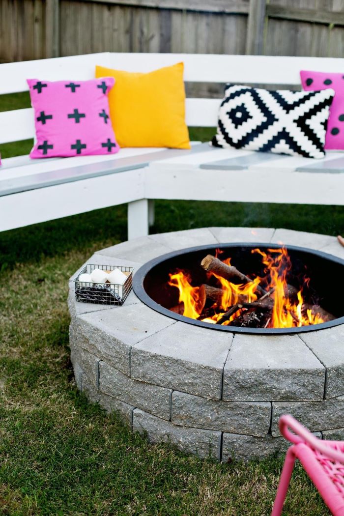 build your own fire pit made of stones white wooden bench with colorful throw pillows around it