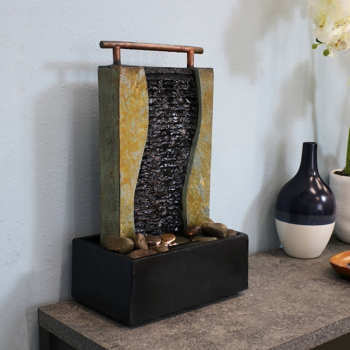 ceramic black pot filled with rocks tabletop water fountain water streaking down from stand light shining into it