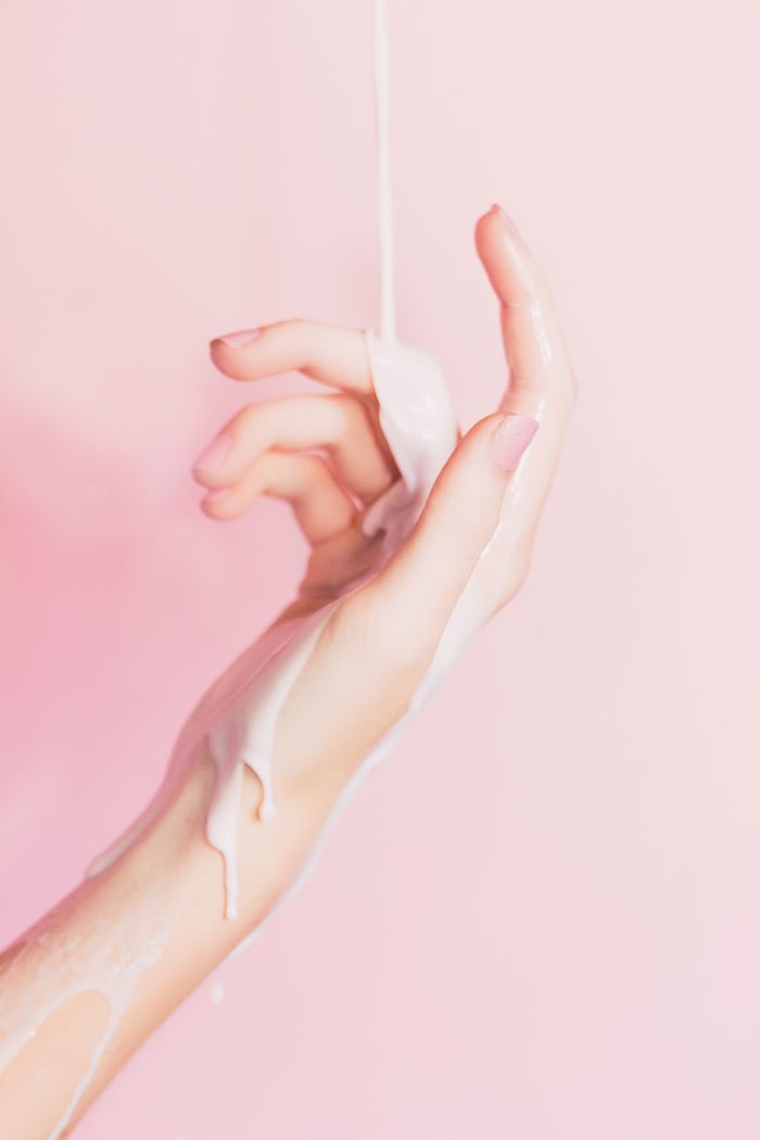 close up photo of female hand with pink nail polish discovering you skin type cream poured on it pink background