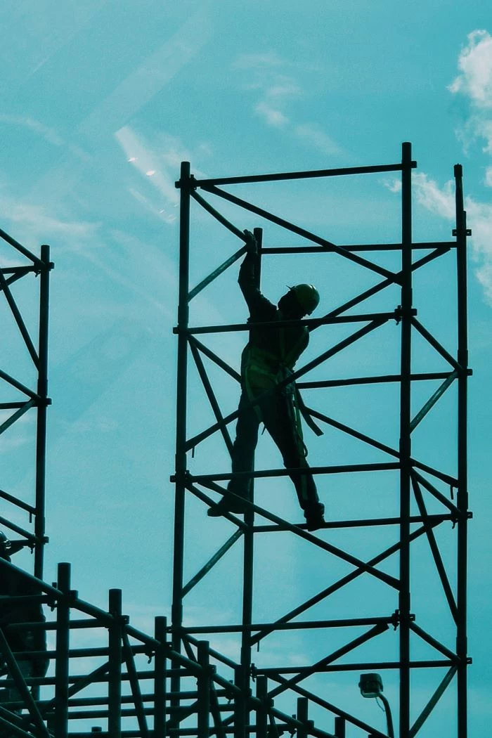 construction worker standing on metal railing construction business ideas blue sky behind him