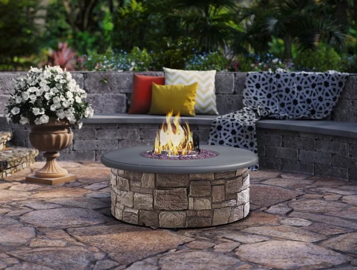 fire burning in round outdoor fire pit ideas made of stone next to bench with throw pillows blanket