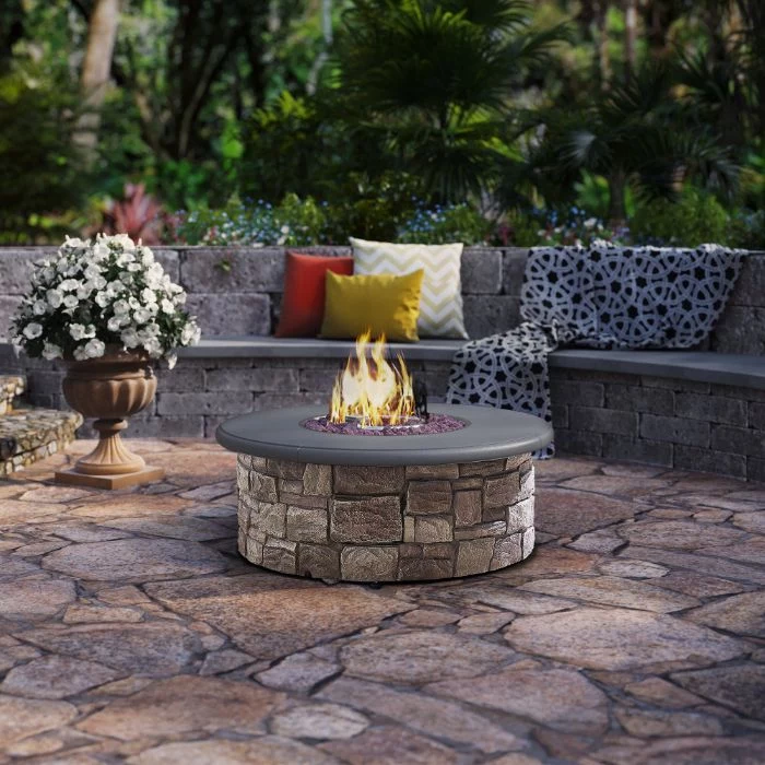 fire burning in round outdoor fire pit ideas made of stone next to bench with throw pillows blanket