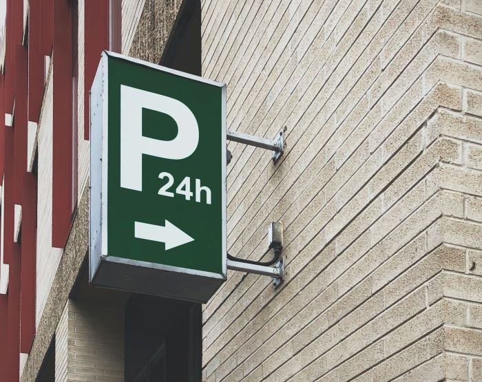 green parking lot sign with twenty four hours sing parking spot in the city hanging on white brick wall