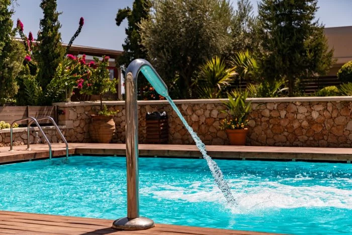 installing a swimming pool fountain water going into pool surrounded by plants and trees