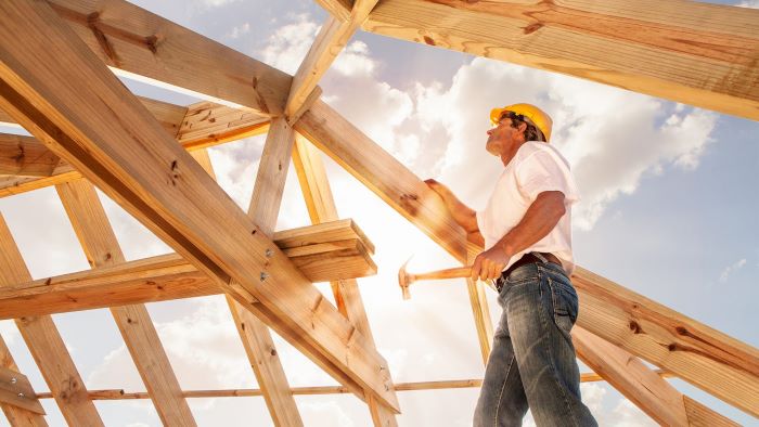 man waring safety hat goggles holding a hammer building your own house standing on the wooden foundations of house