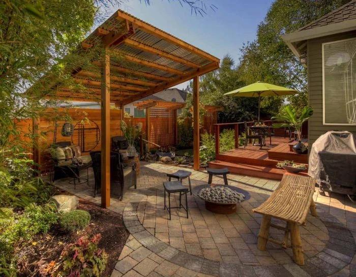 pergola with garden furniture underneath in ground fire pit small stools arranged around metal fire pit filled with stones