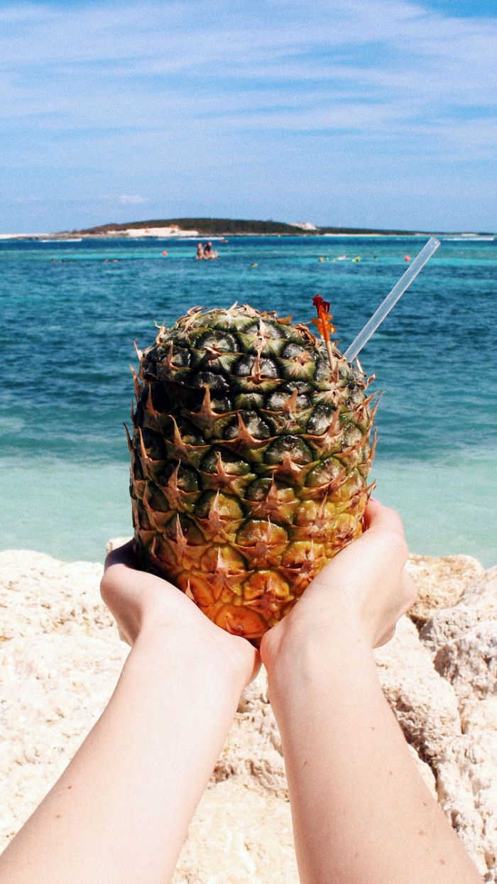 pineapple with straw being held by two hands summer wallpaper hd ocean in the background
