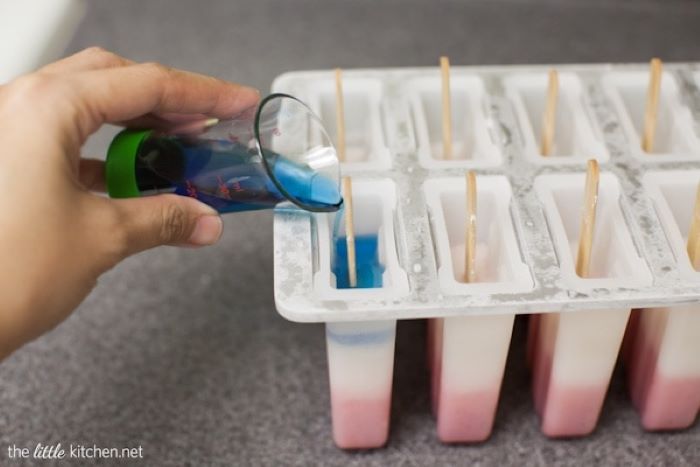 pouring blue sugar water into the popsicle mould 4th of july dessert recipes red white and blue popsicles