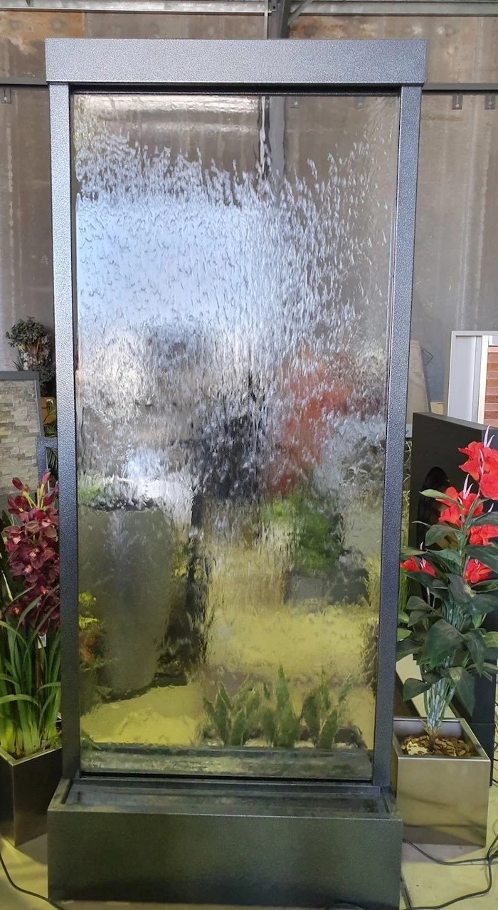 small water fountain made of glass water streaking down the glass surrounded by flowers