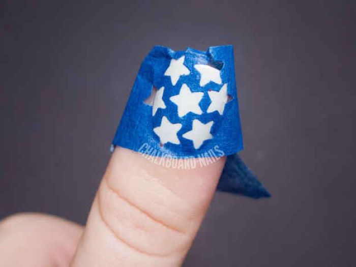 stencil of stars placed on top of nail with white nail polish red white and blue nail designs