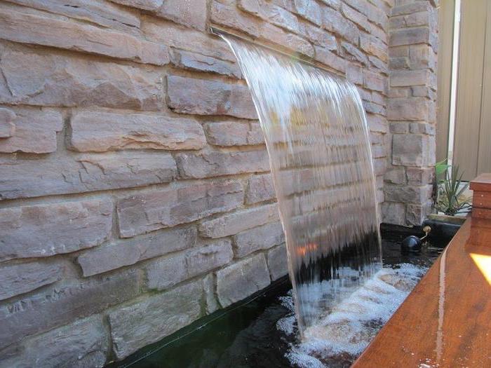 stone wall waterfall coming out of it wall water fountain water falling into small pond