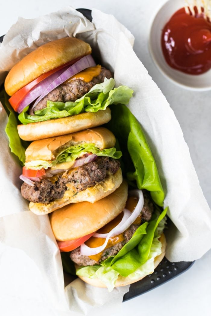 three burgers wrapped in paper placed inside baking tray best burger recipe bowl of ketchup on the side