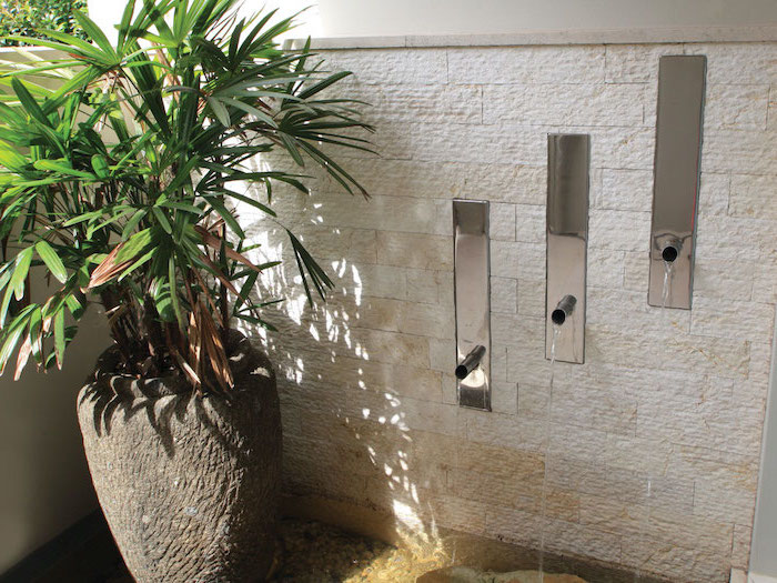 three water tabs on wall with stone bricks indoor water fountain potted plant on the side