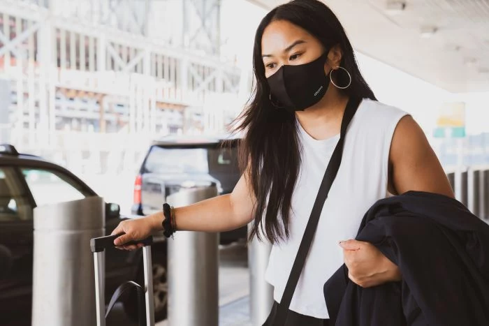 travel tips woman with long black hair wearing white top face mask carrying luggage