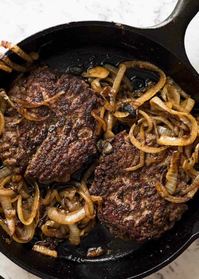two patties cooking with onion in black skillet how long to cook burgers placed on marble surface