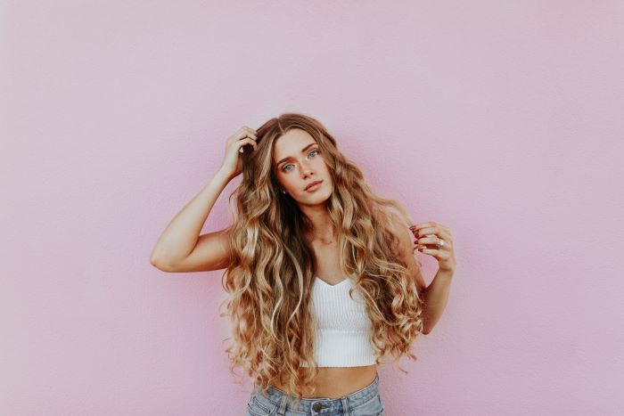 woman with very long blonde wavy hair avoid bad hair days wearing white crop top jeans