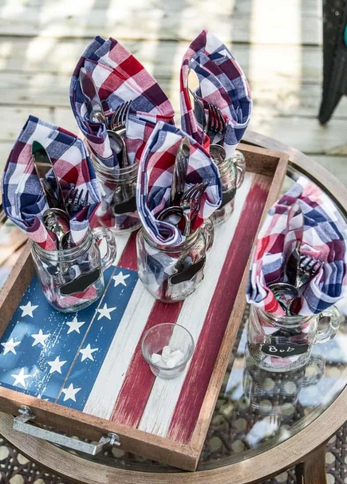 wooden board with american flag painted on it 4th of july decorations red white blue napkins inside jars with fork spoon knife