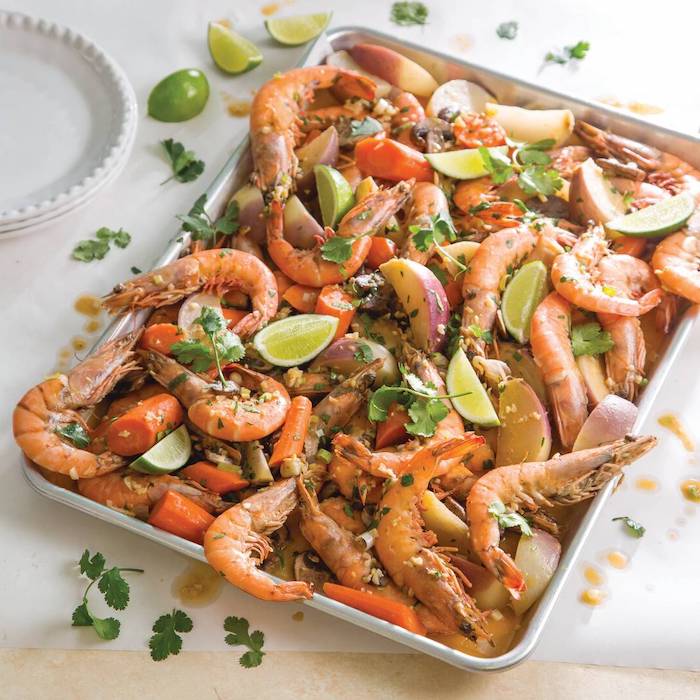baking sheet filled with shrimp carrots potatoes lime wedges garnished with parsley seafood boil sauce