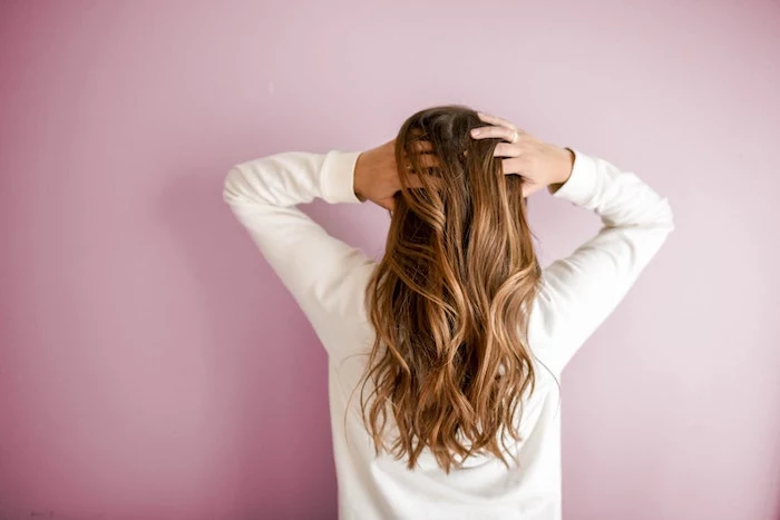 best hair mask woman with long light brown caramel wavy hair wearing white blouse pink background