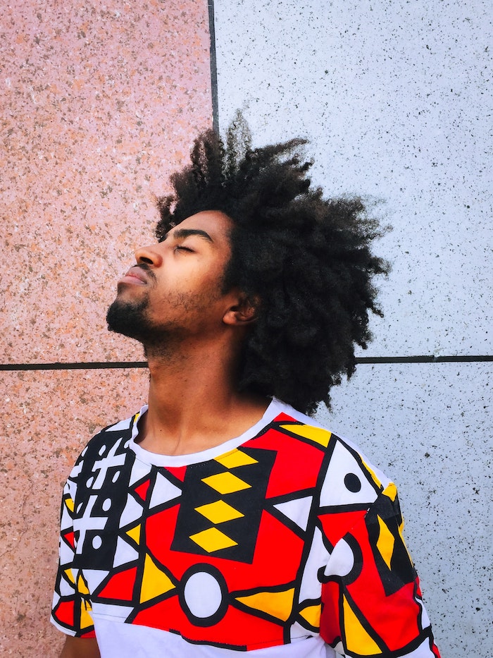 black curly hair on man wearing colorful t shirt diy deep conditioner standing in front of granite tiled wall