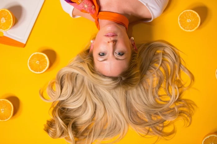 blonde woman laying on yellow surface hair spread out homemade hair mask lemons around her