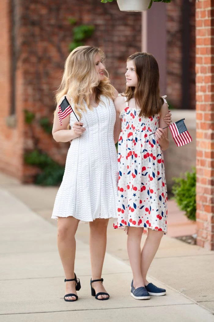 blonde woman wearing white lace dress girl wearing red white and blue dress baby boy 4th of july outfit holding american flags