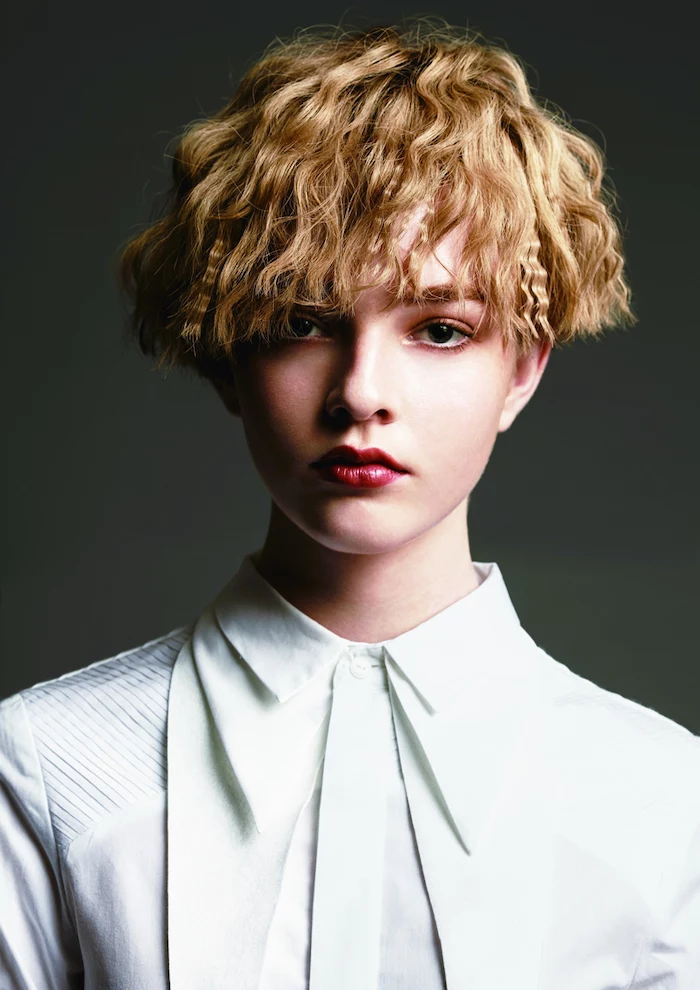 blonde woman with short crimped hair wearing white shirt red lipstick phootographed on black background