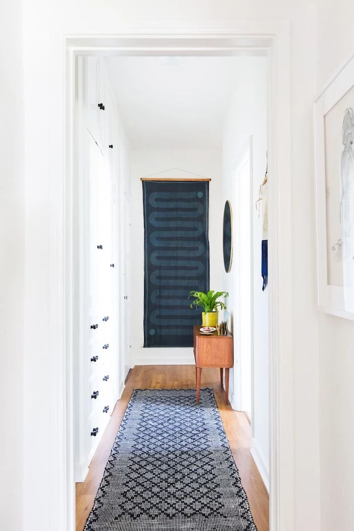 blue fabric art hanging on white walls hallway wall decor blue rug on wooden floor wooden cupboard