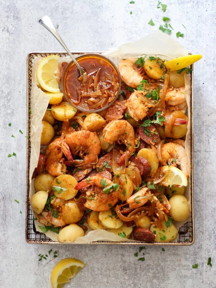 cajun seafood boil paper lined baking sheet filled with shrimp potatoes lemon wedges sauce in a bowl on the side
