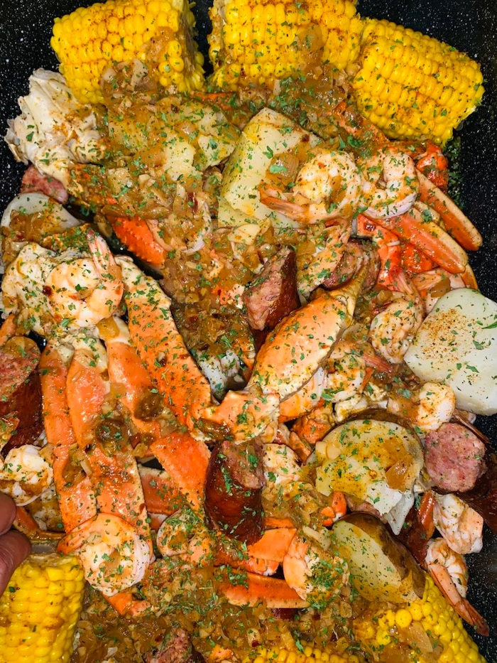 close up photo of how to make a seafood boil corn on the cob sausages potatoes garnished with chopped parsley