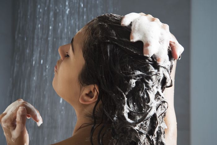 coconut oil hair mask woman under the shower with water running rubbing shampoo in her hair