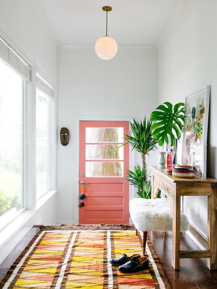 colorful rug on wooden floor decorating ideas for stairs and hallways pink door white walls tall windows framed art potted plants boho style