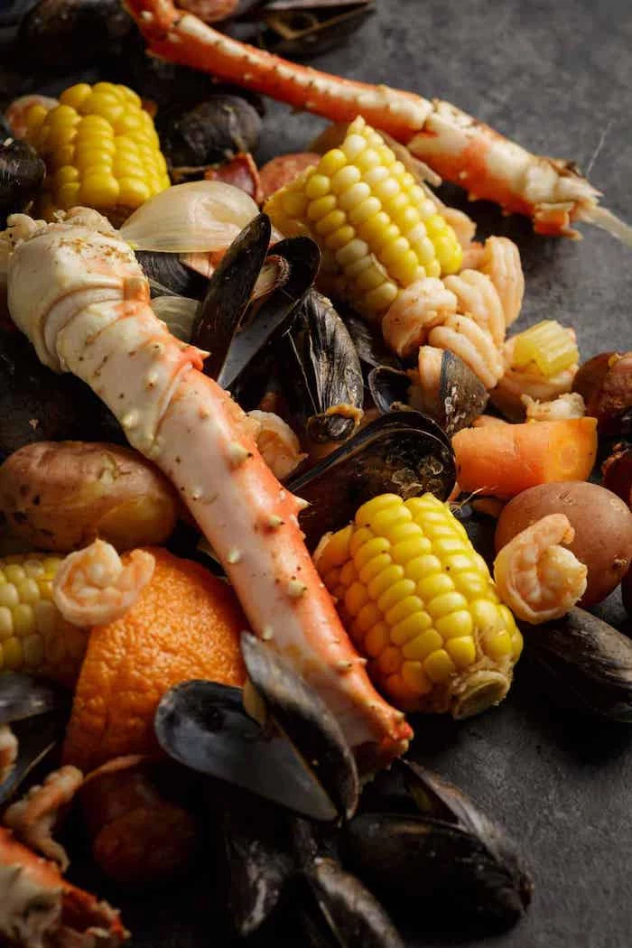corn mussels shrimp crab boil seasoning potatoes carrots placed on black surface