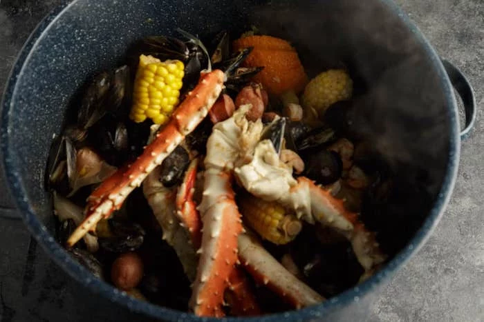crab boil seasoning with corn mussels potatoes all placed in pan in boiling water