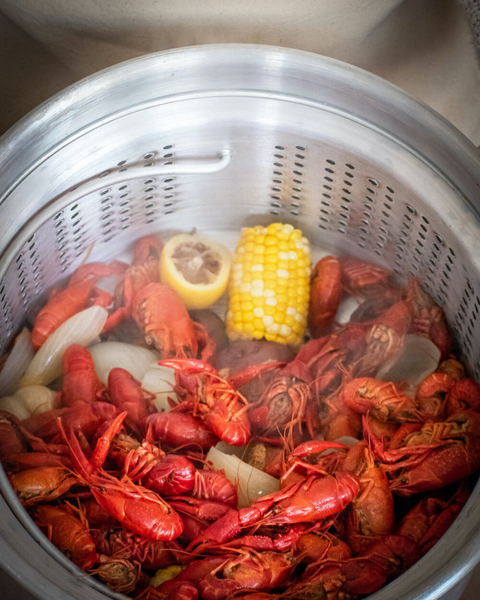 crawfish boil crab boil seasoning inside big pan with onion potatoes corn on the cob lemon wedges