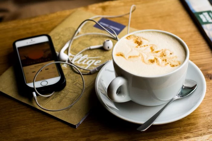 cup of coffee placed on wooden table lifestyle podcast examples phone next to it with plugged in headphones