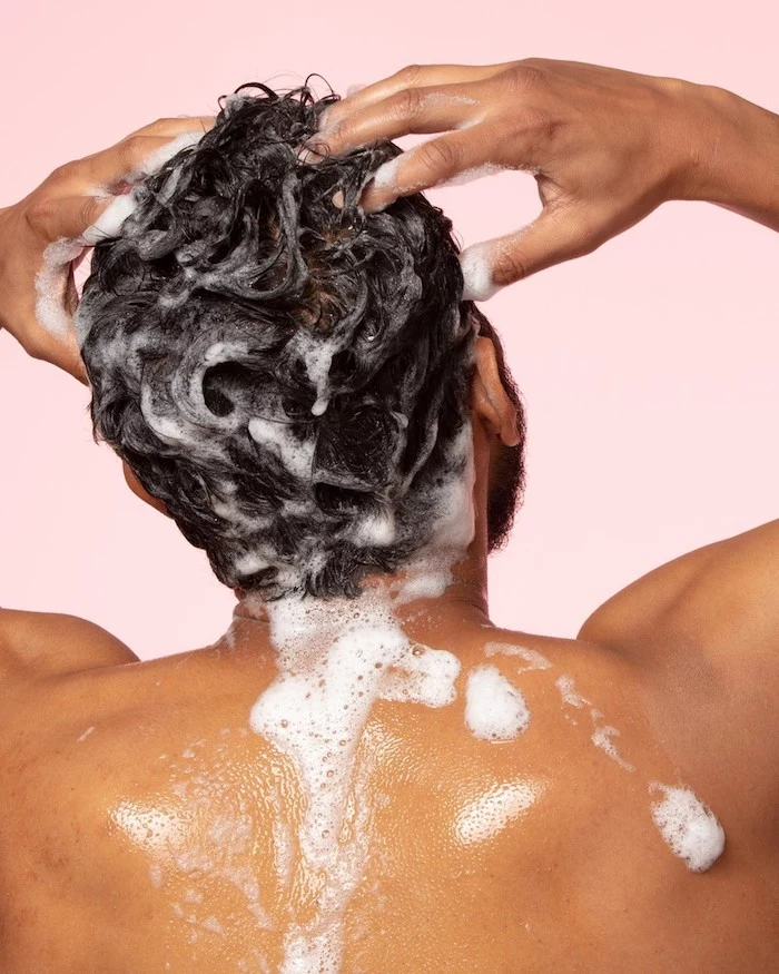 diy hair mask man under the shower rubbing shampoo on his hair pink background