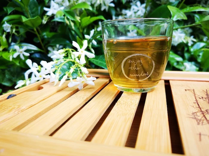 green tea inside glass placed on wooden surface home remedies for dry hair white flowers around it