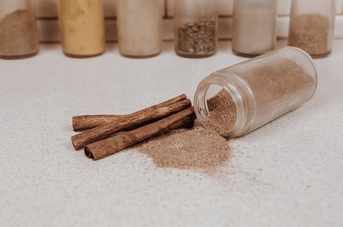 home remedies for dry hair cinnamon in jar spilled onto white surface cinnamon sticks on the side