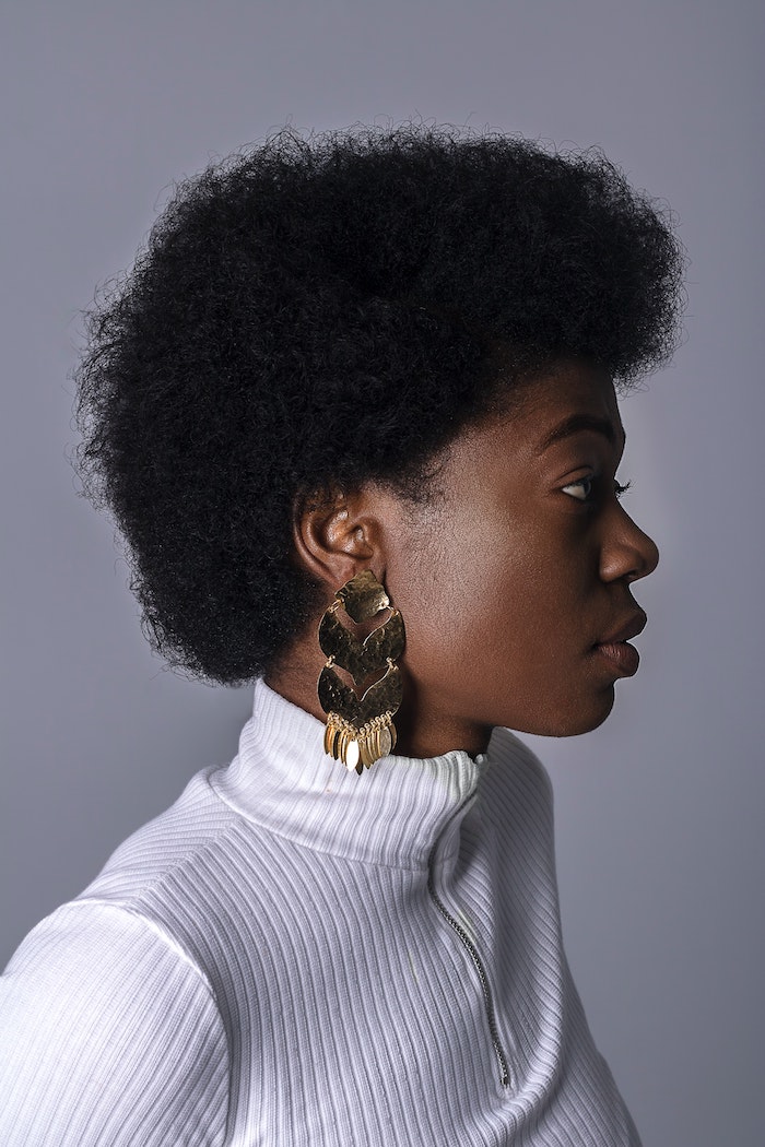 homemade hair mask woman with very short curly hair afro wearing white polo blouse gold earrings