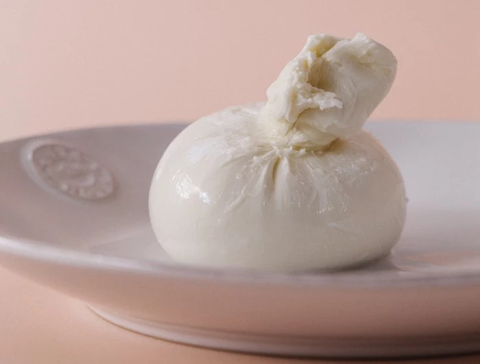 italian burrata cheese wrapped in fine fabric placed on white paper on pink background