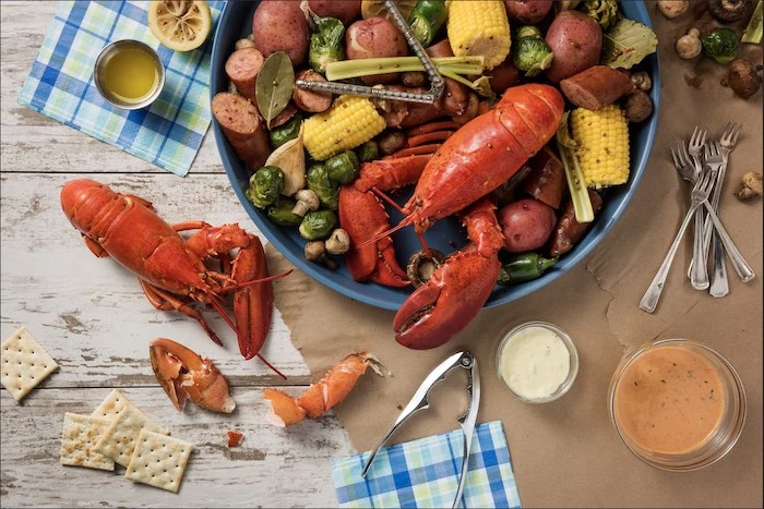 lobster crawfish crab boil recipe placed on white wooden table with potatoes artichoke corn on the cob
