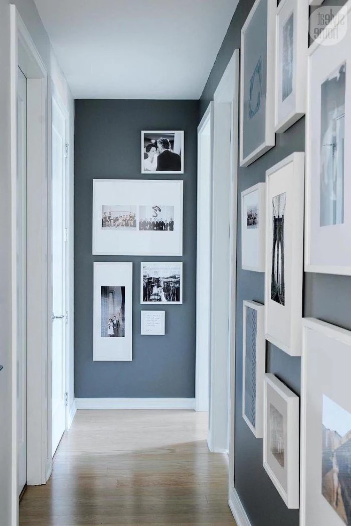 lots of photos and art in white frames of different sizes hanging on dark blue walls narrow hallway ideas
